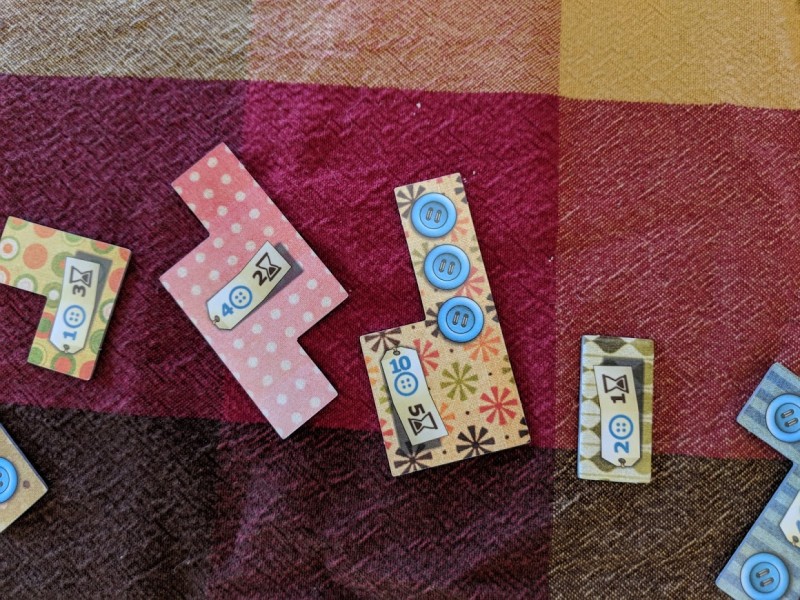 Game pieces from Patchwork, each displaying a button cost and a "time" cost. One patch has three buttons on it.