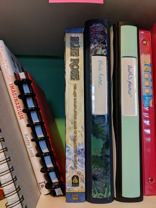 A bookshelf with a number of books on it, including the Blue Rose book and a binder labeled Blue Rose.