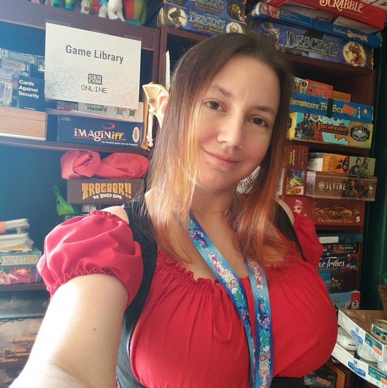 Me dressed as Elinyr, in front of a bookshelf full of games with a sign saying "Games Library" taped to it.