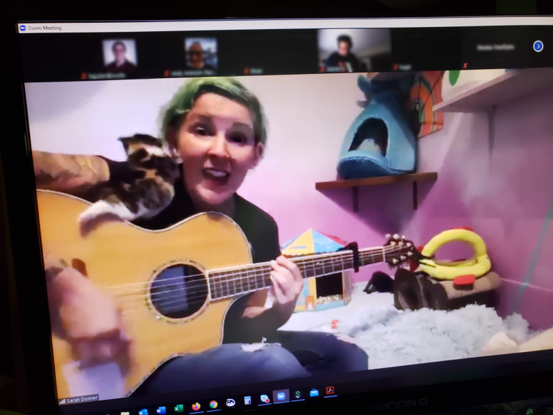 Sarah Donner playing the guitar with a kitten trying to climb on her.